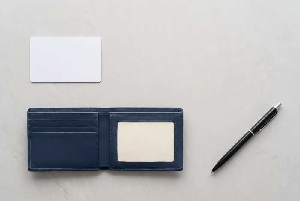 Generated image: a blank white plastic card, an open dark blue wallet, a blank card face down and a pen on a pale grey counter; not a real card.